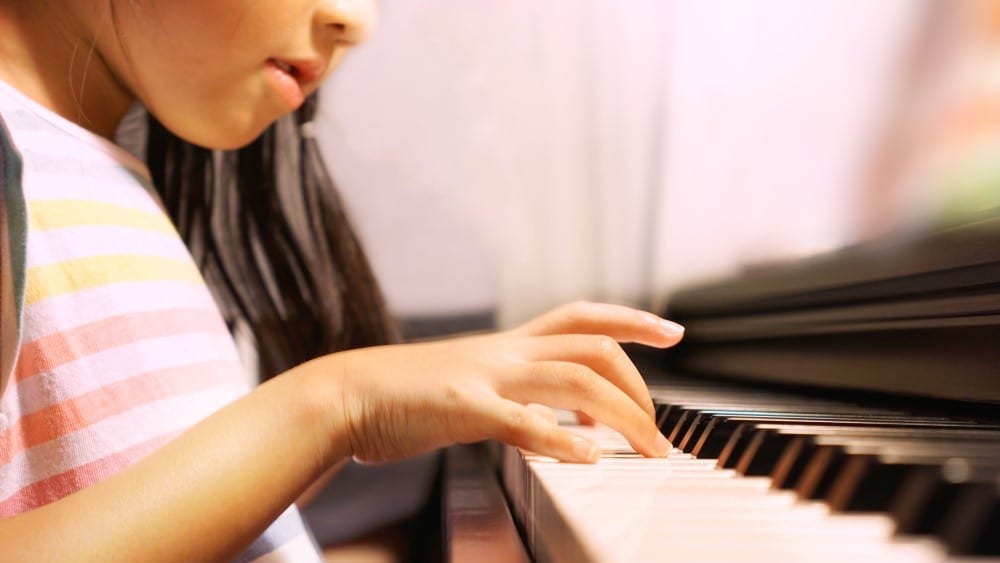 Bright, soft shot of Asian little girl happily playing keyboard piano during her practice at home
