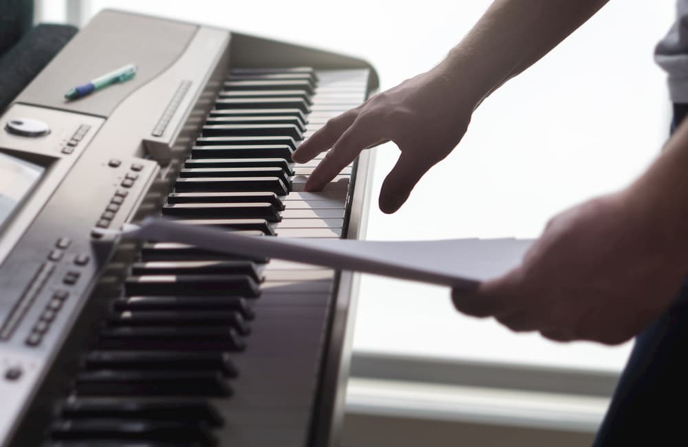 One single finger pressing key on piano. Man looking at paper notes and training a new song or melody from the sheet music. Pianist composing new work or creative producer working in home studio.