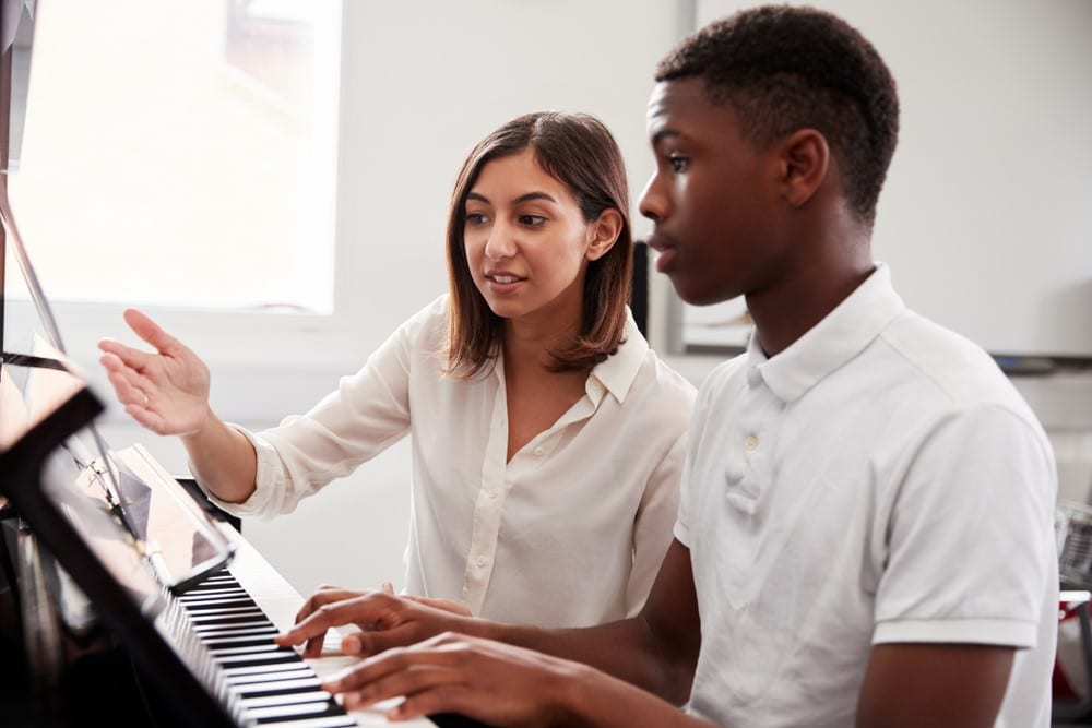 Male Pupil with Teacher Playing Piano in Music Lesson